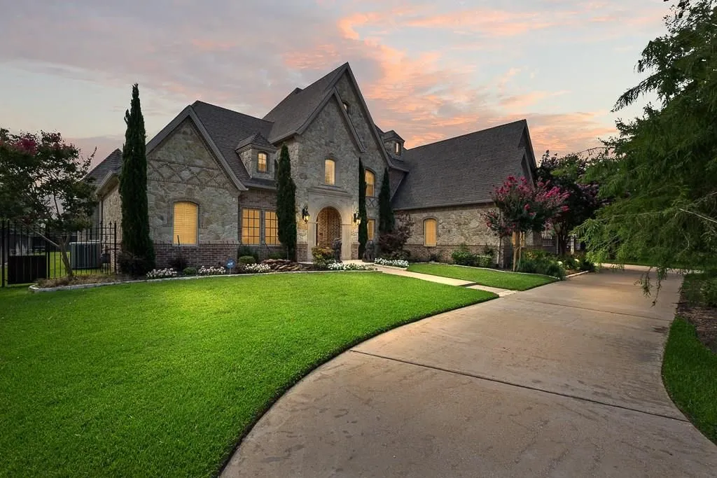 Stone two-story house at dusk with a long driveway and green lawn